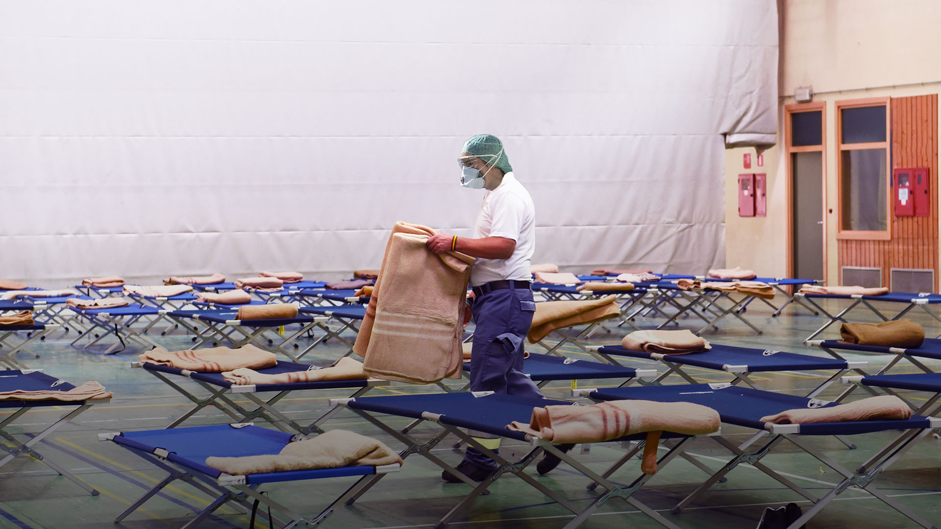 Man working amongst cots in a gym