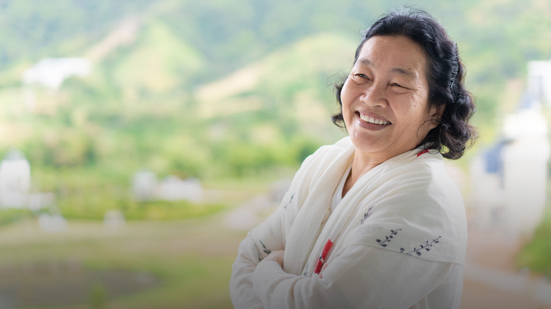 Asian elderly woman wear a white cloth is standing and smiling in the background of green mountain background.