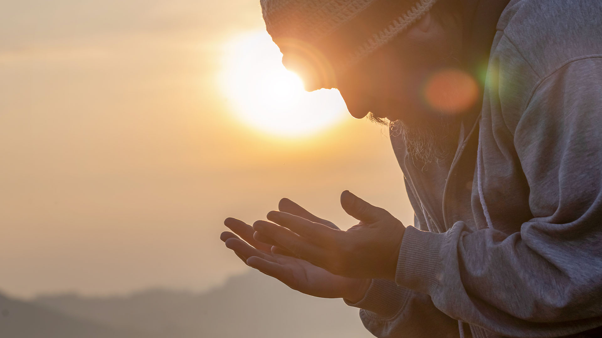 Man praying to God with sun setting in background