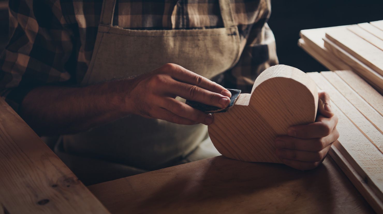 man sanding down a wooden heart