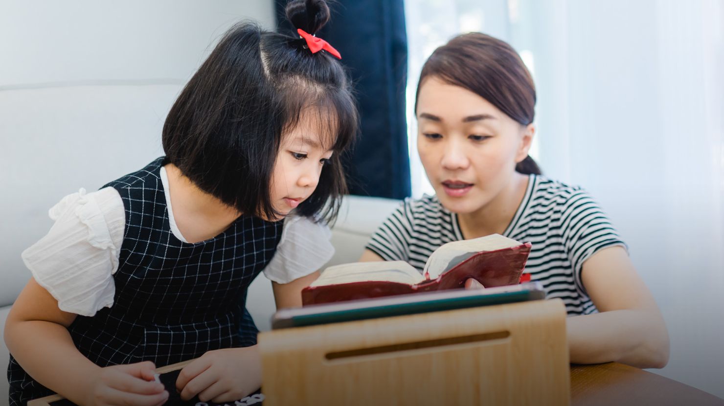 Mom and daughter reading holy bible at home.