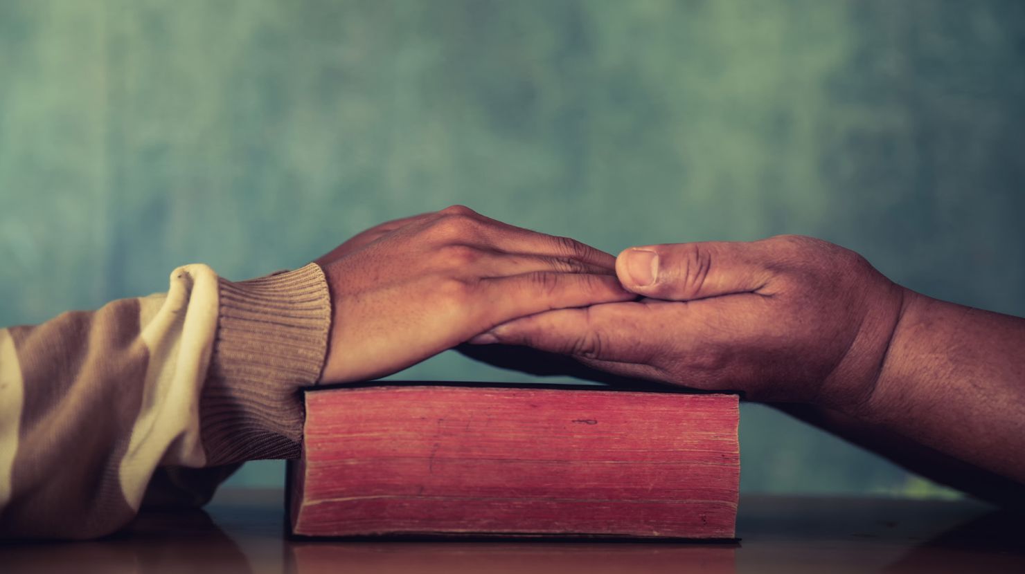 People praying together. Hands over bible.