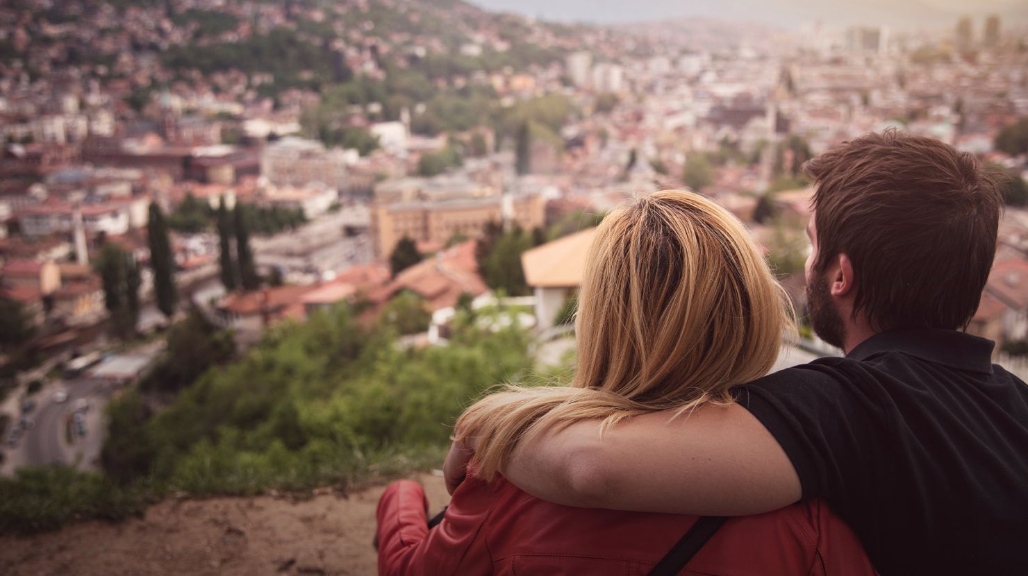 Young couple sitting on a hill watching the city of Sarajevo beneath them