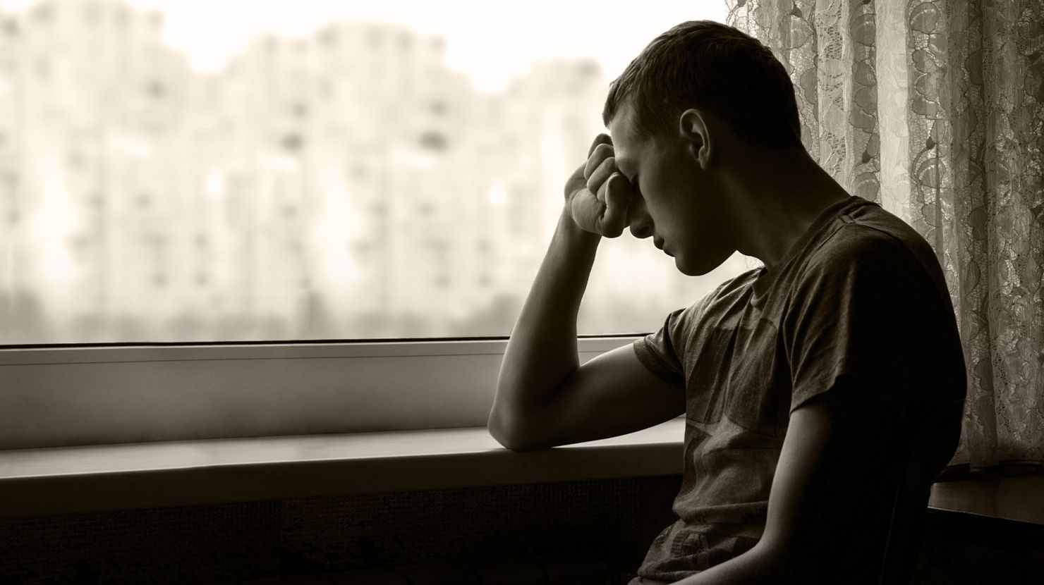 Boy sitting sadly by a window