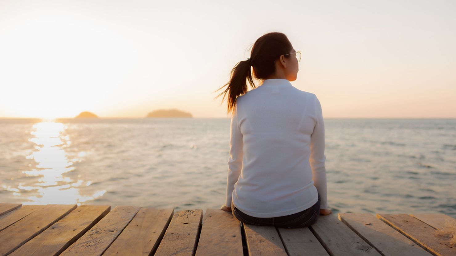 Lonely woman sitting on a wooden bridge sunset.