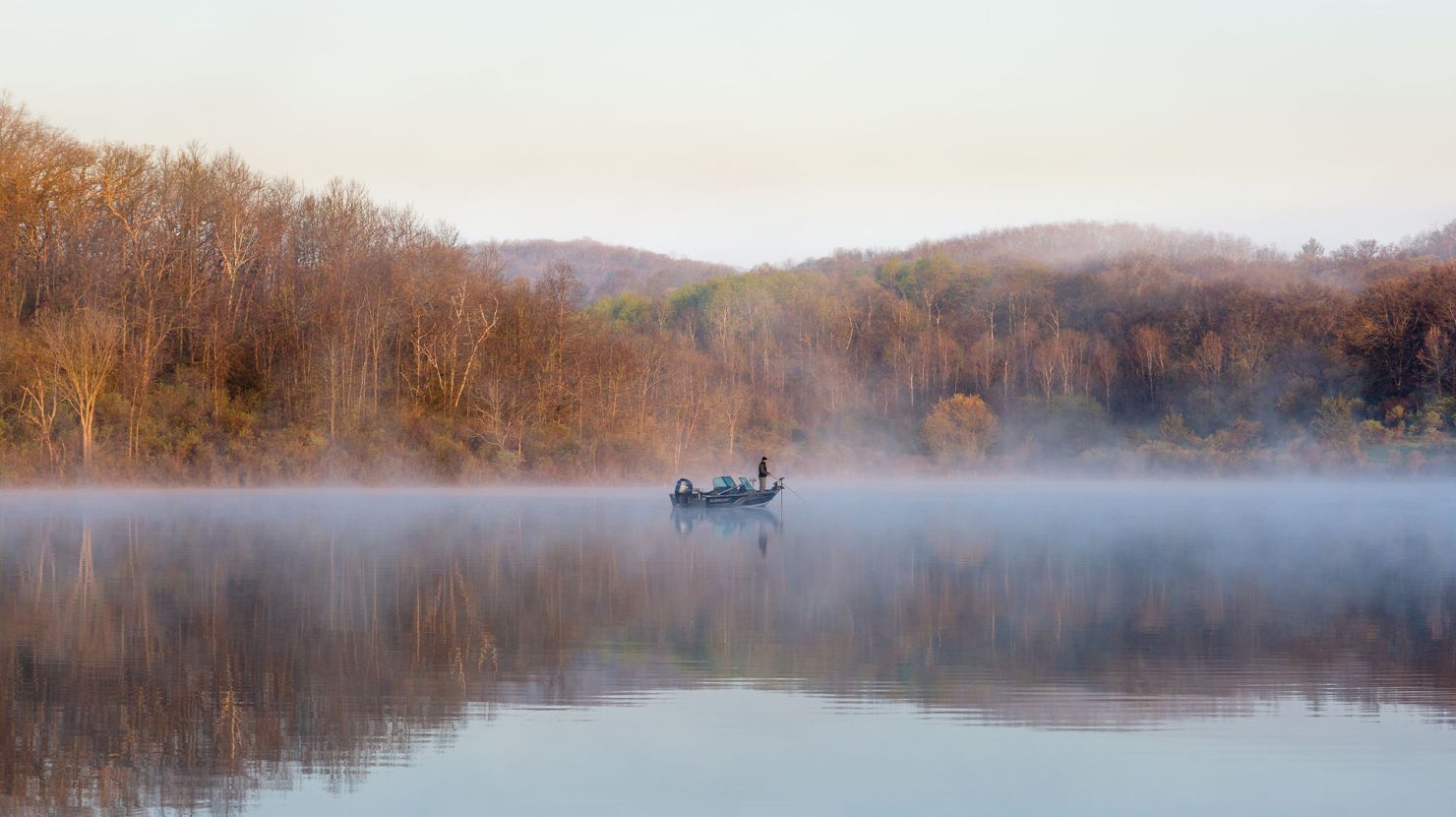 Man in distance fishing on large reflective lake