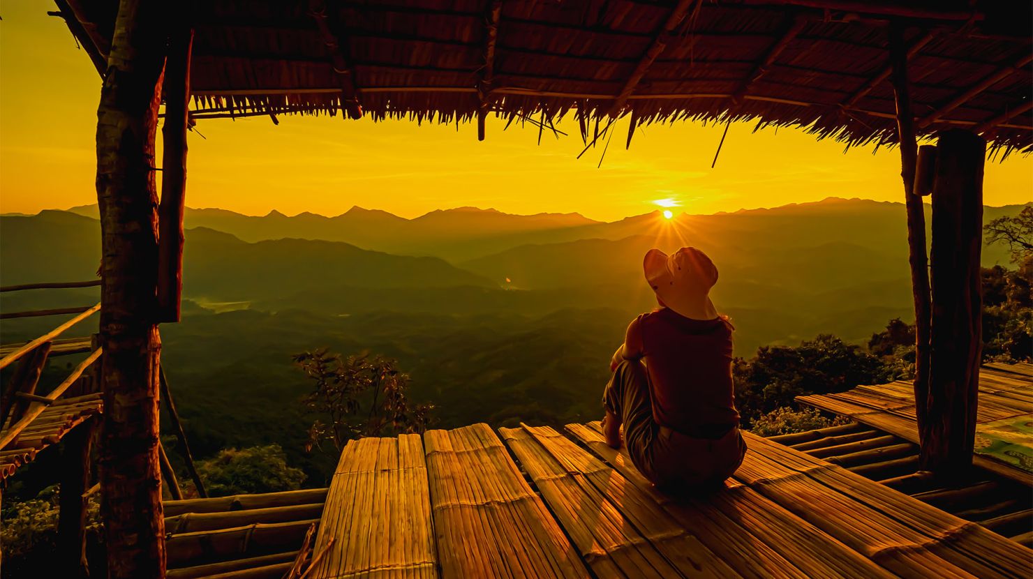 A woman, sitting on a porch, looking out onto a sunset